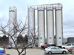 4 silver silos with ALPLA logo on top of each, positioned behind a parking lot