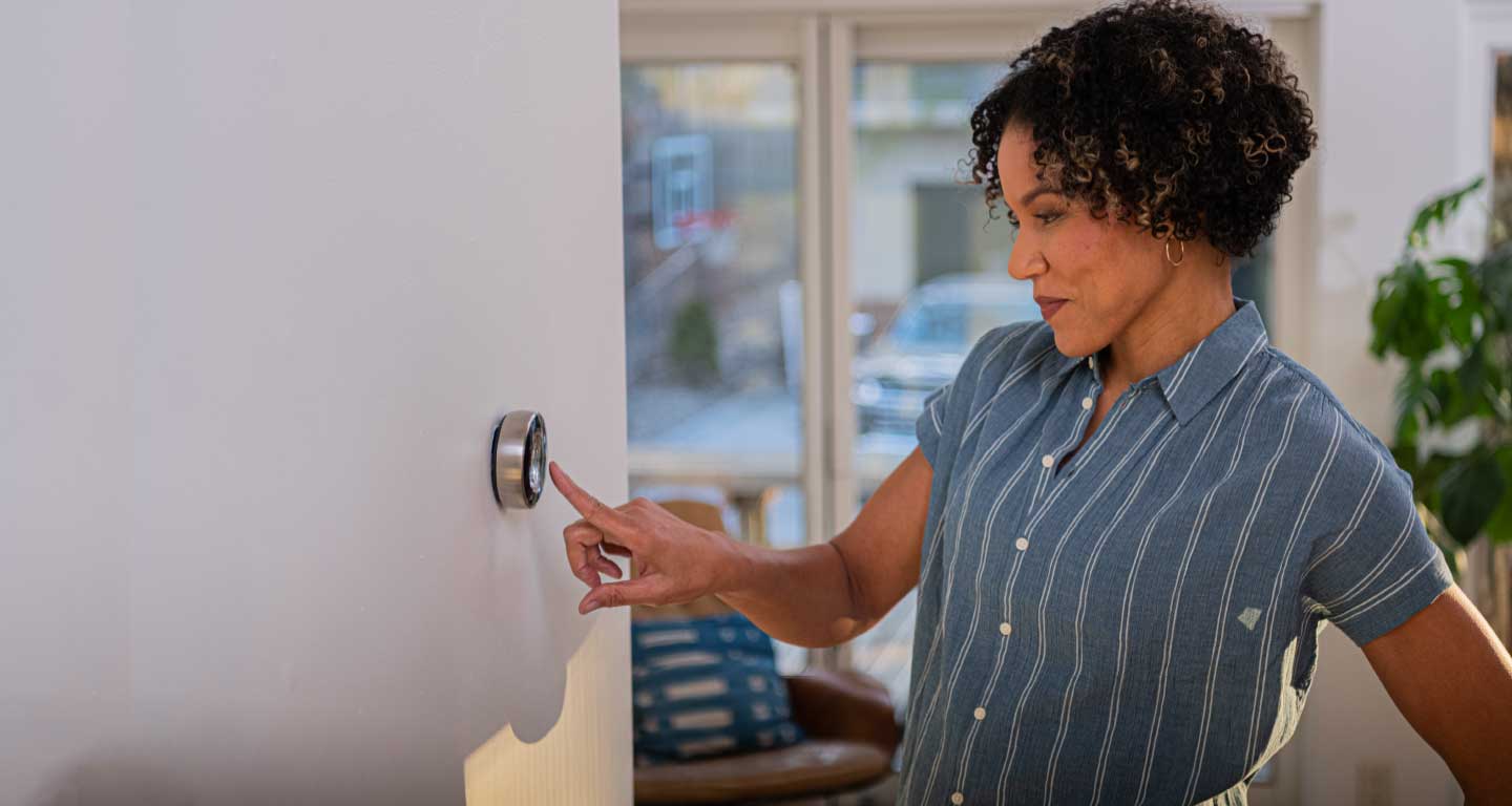Black women wearing blue shirt, using smart thermostat