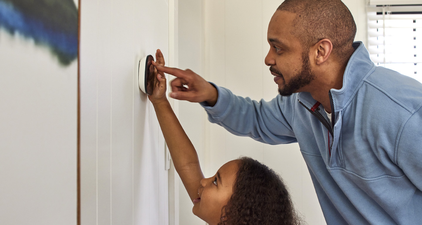 Black father and daughter using a smart thermostat