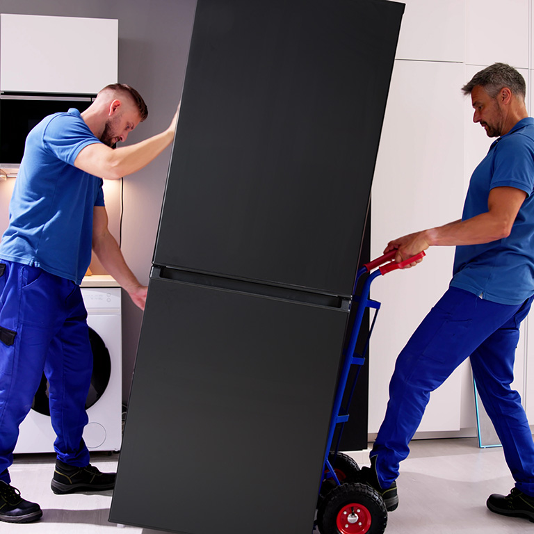 Two men with a two-wheeled dolly removing a refrigerator from a kitchen.