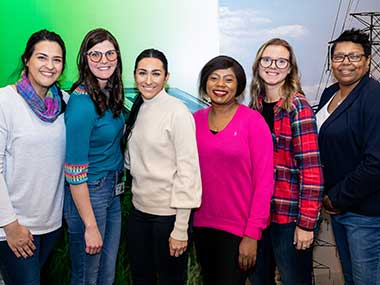 Six women, all MidAmerican employees, standing in front of a mural