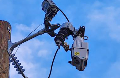 TripSaver device installed on a power line, mounted high on a utility pole against a clear blue sky