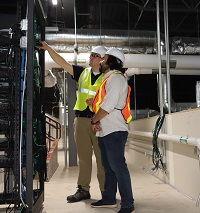 Two men in vests and hard hats looking at an energy management system in the control room of a building