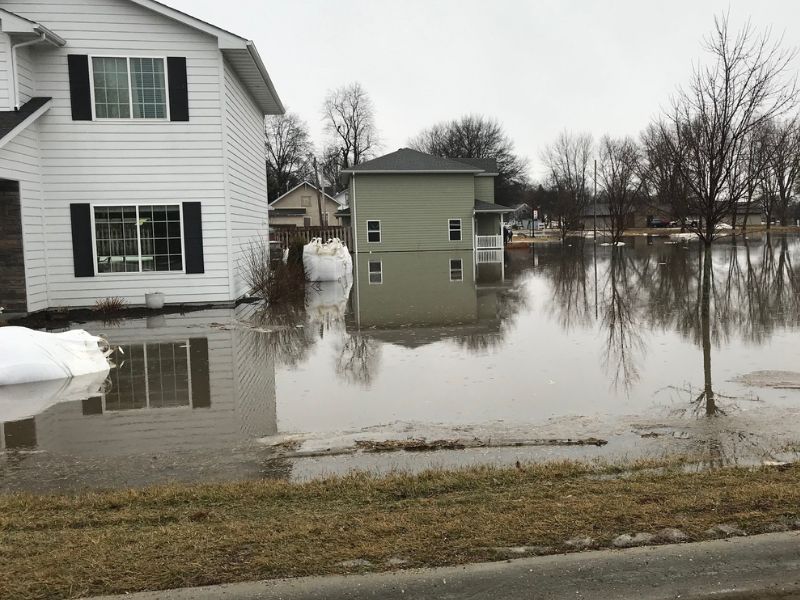 A flooded residential neighborhood showing multiple houses with flood water covering most of the lawn