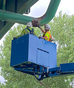 Two MidAmerican employees in the elevated bucket of a truck inspecting a natural gas line under and overpass
