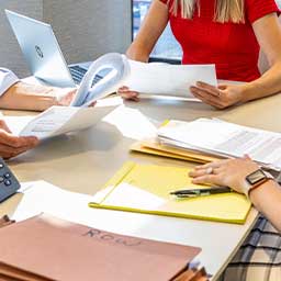 Photo of desk covered in paperwork with three people seated