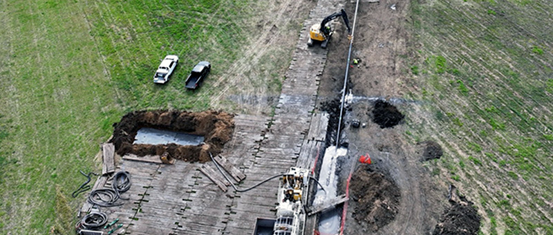 An aerial photo of a worksite near the Rock River in Illinois with crews repalcinf pipes and excavated land with multiple vehicles