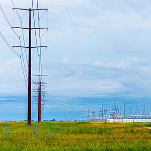 High voltage transmission lines running from the foreground to an electrical substation structure in the background