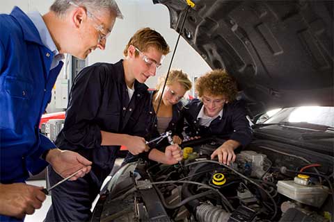 Students and there teacher working on a car engine