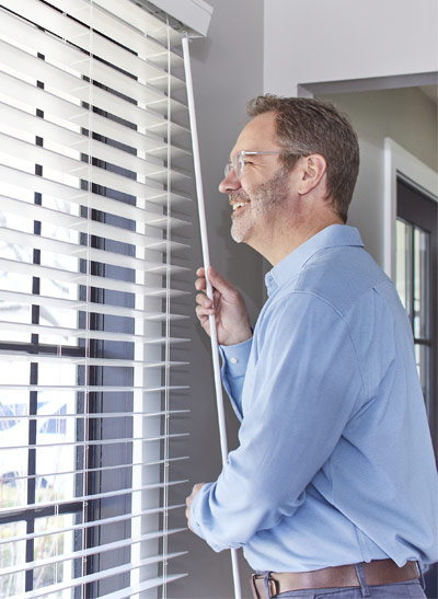 Man looking through his window while adjusting the blinds