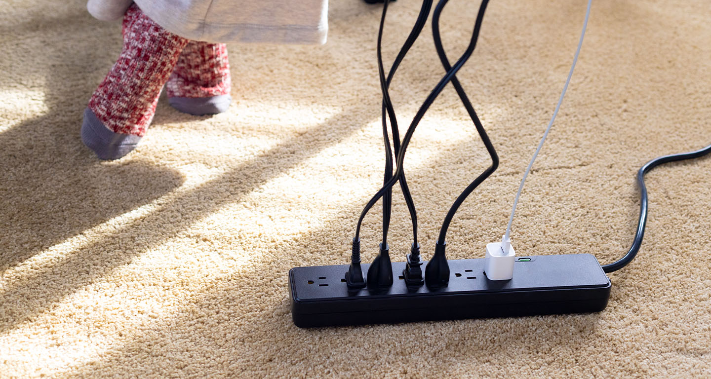 Close-up of a power strip with five power cords plugged in on a carpeted floor
