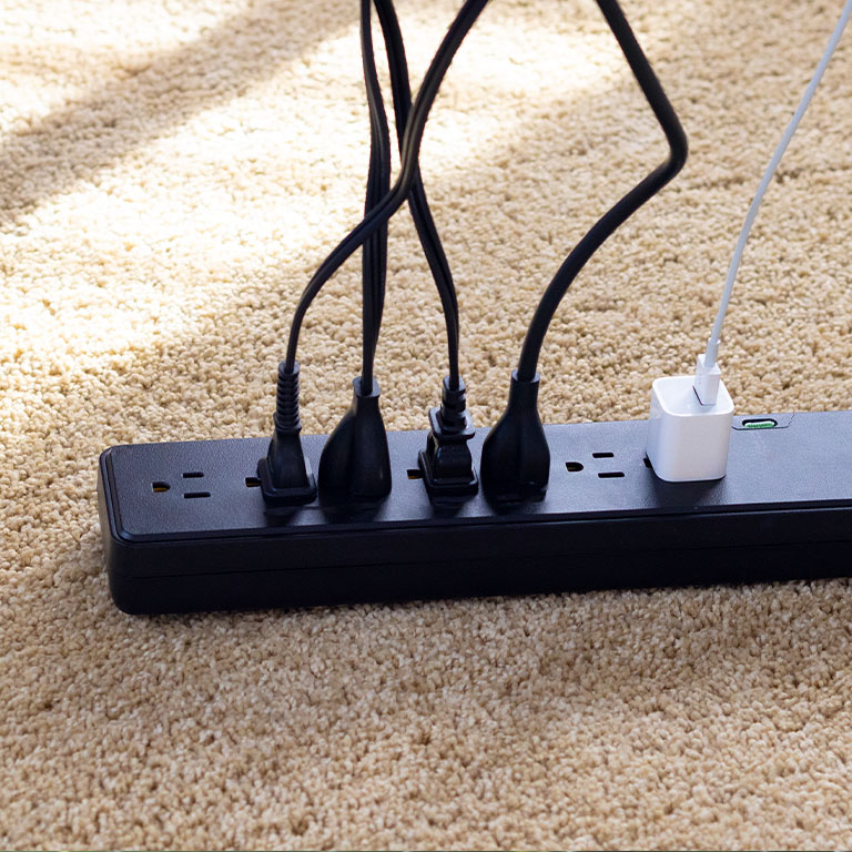 Close-up of a power strip with five power cords plugged in on a carpeted floor
