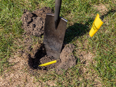 close-up of a shovel digging a hole in a yard; a yellow gas line is exposed in the hole