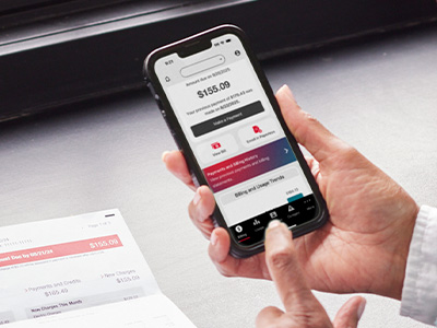 Hand holding a mobile phone displaying the MidAmerican mobile app bill due screen with a corresponding paper bill shown below and in the background.