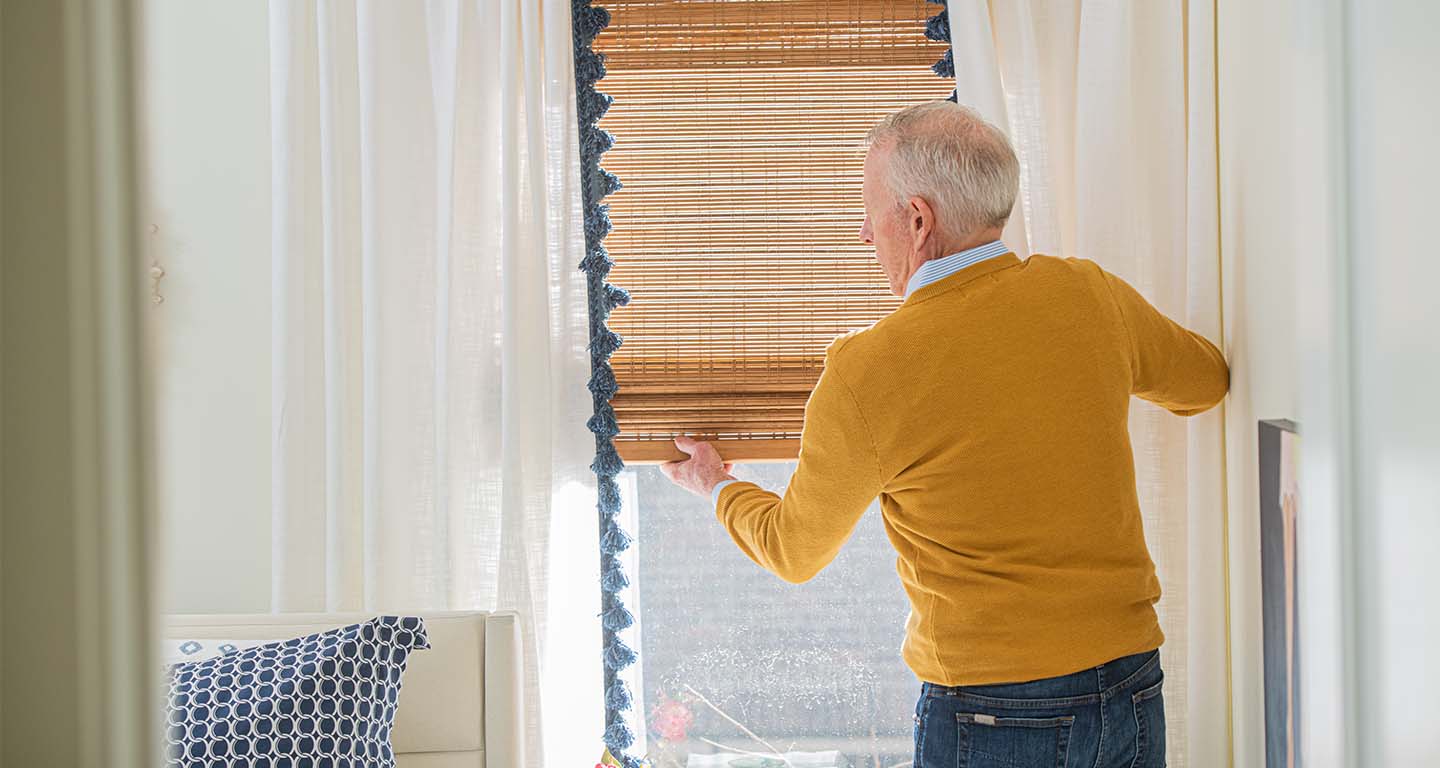 Senior man opening blinds to let in warm sunlight