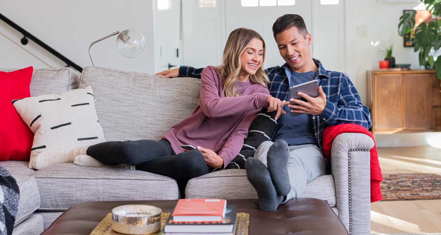 Young woman, man sitting on couch looking at tablet