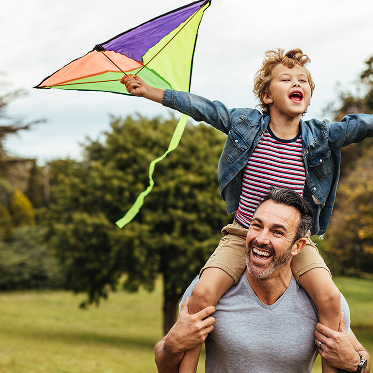 A father carrying his son on his shoulders as they fly a kite