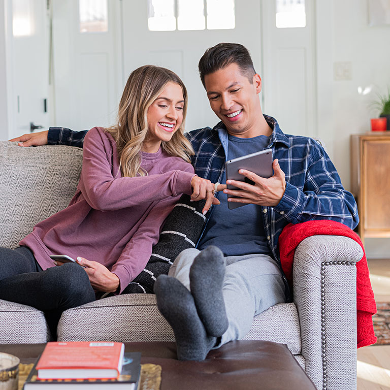Young woman, man sitting on couch looking at tablet