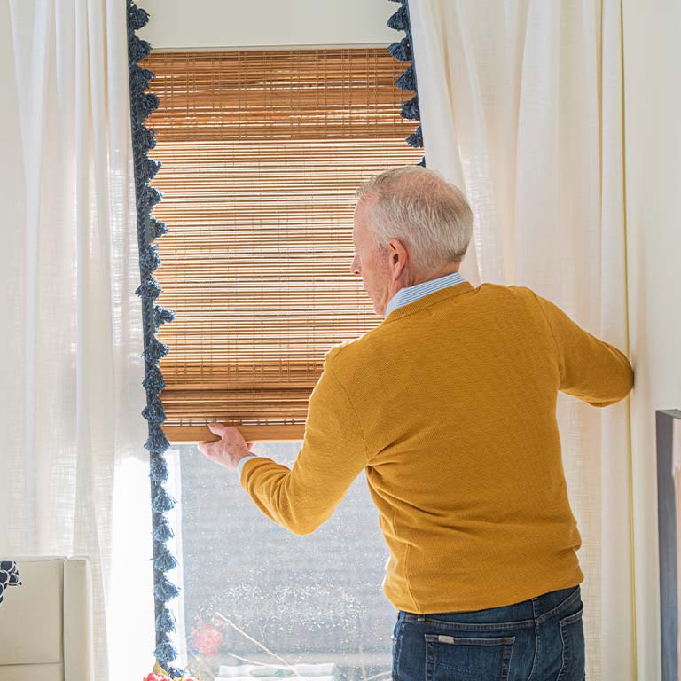Senior man opening blinds to let in warm sunlight