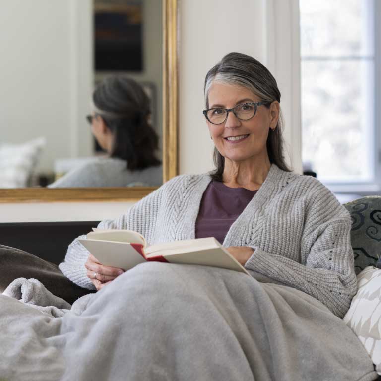 Older women cuddled up on the couch reading under a blanket