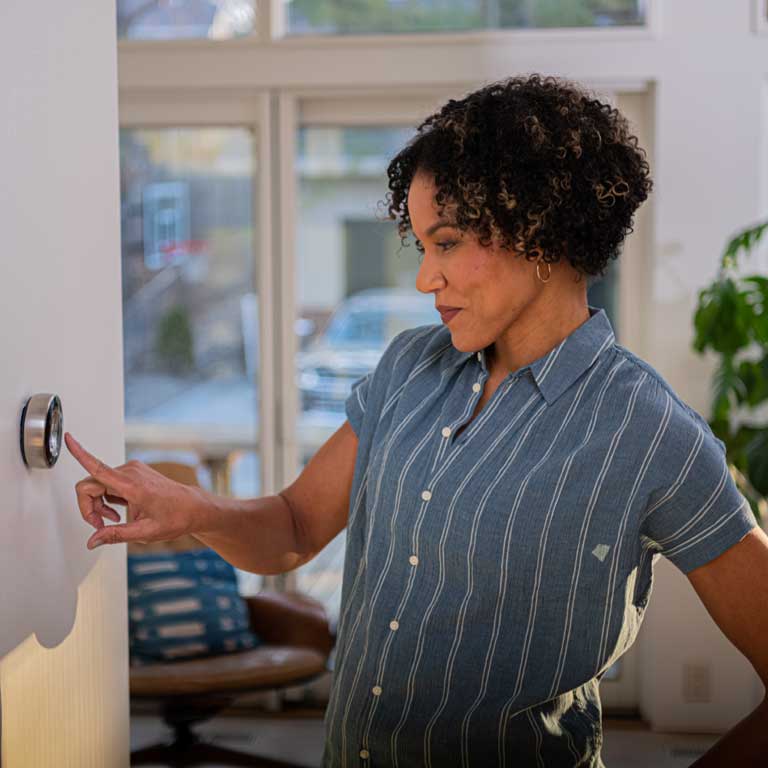 Black women wearing blue shirt, using smart thermostat