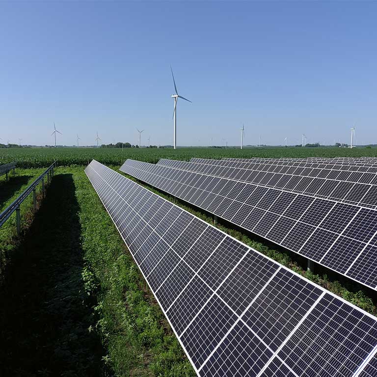 Side view of rows of solar panels, wind turbines in background