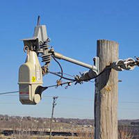 TripSaver device installed on a power line, mounted high on a utility pole against a clear blue sky