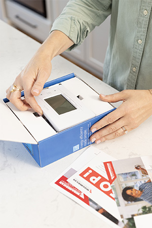Close-up image on a woman's hands removing a new smart thermostat from its box, with MidAmerican collateral material in the foreground