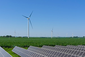 Solar arrays in the foreground, next to a green field with several wind turbines extending into the distance.