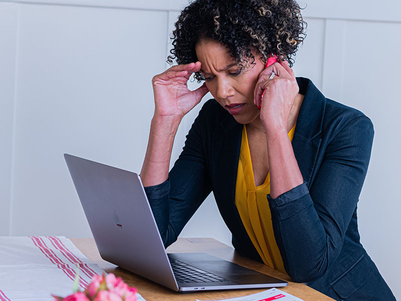 Frustrated woman looking at a computer while speaking on a mobile phone.