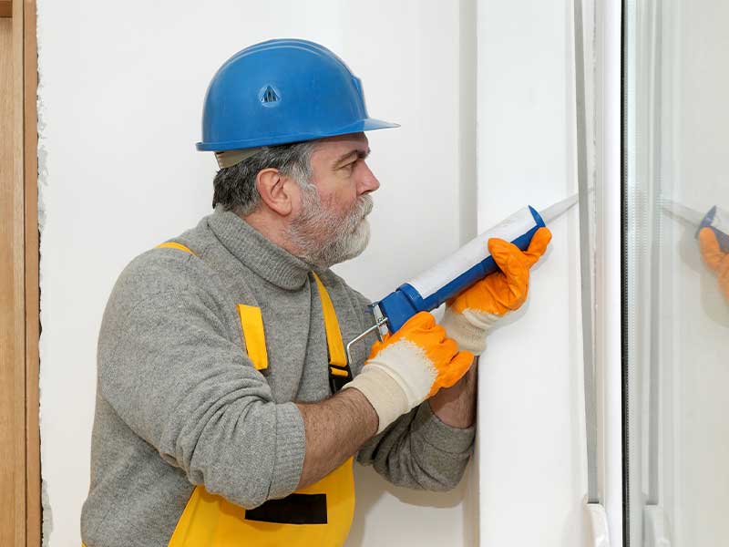 Worker sealing windows with caulk