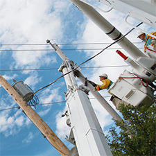 Worker in a bucket truck performing work on a utility pole with overhead wires