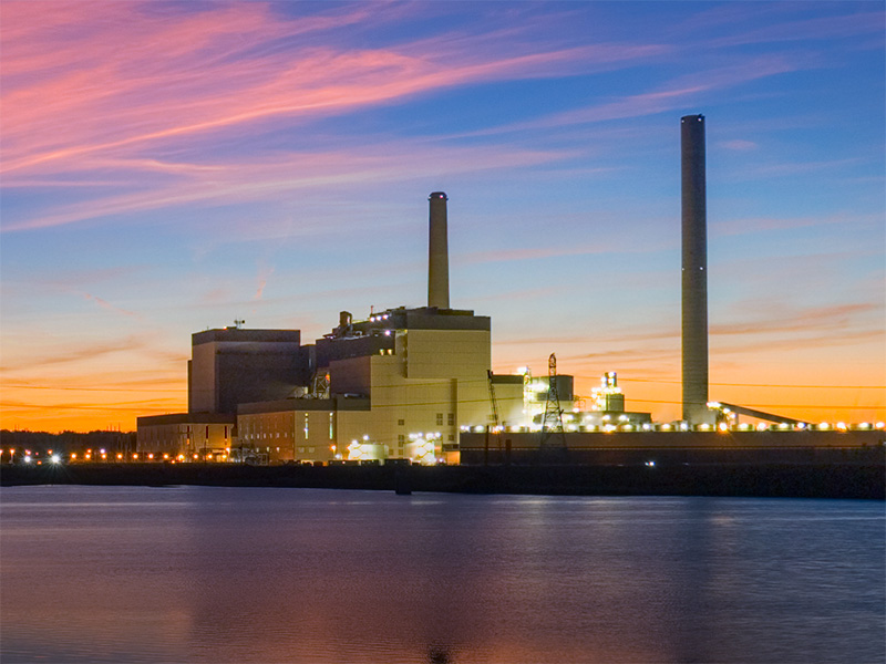 Photo taken across the river of the Walter Scott, Jr. Energy Center with the sun setting behind it and colors reflecting in the water.