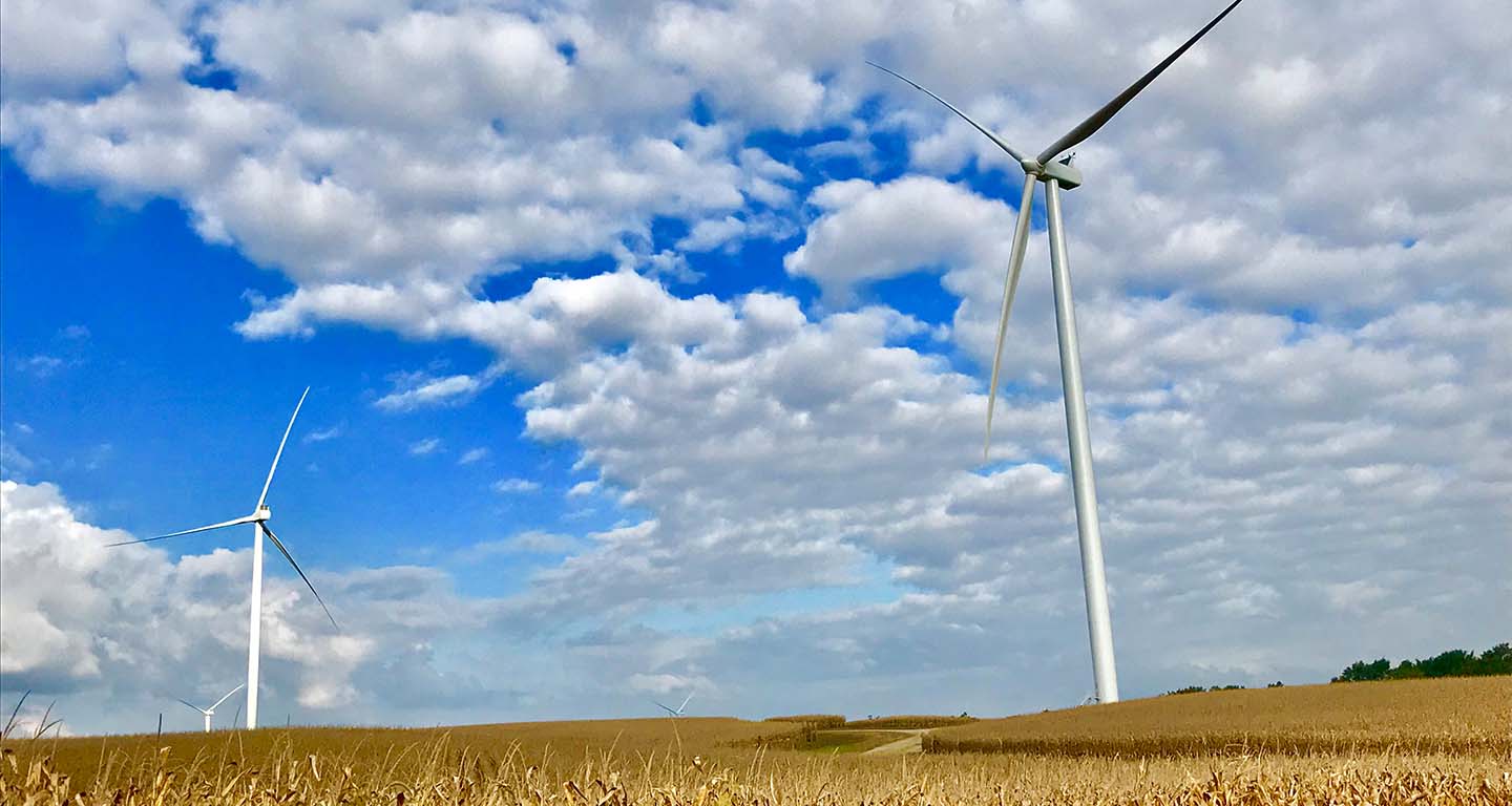 MidAmerican wind turbines on a farmland under a blue, cloudy sky