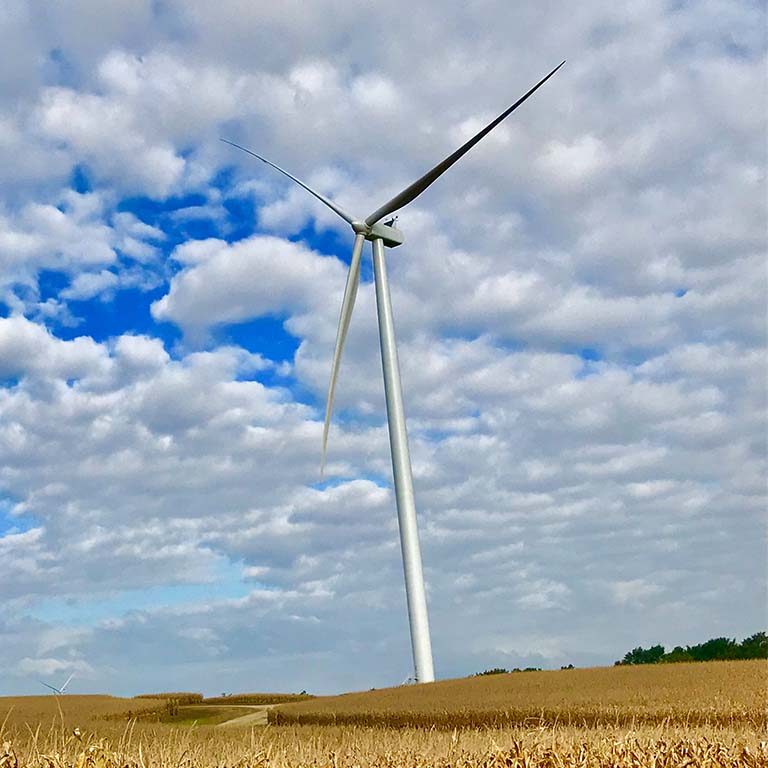 MidAmerican wind turbines on a farmland under a blue, cloudy sky