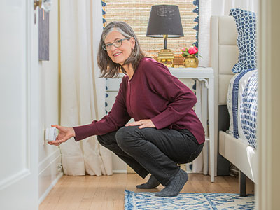 Lady squatting in bedroom plugging in CO detector 